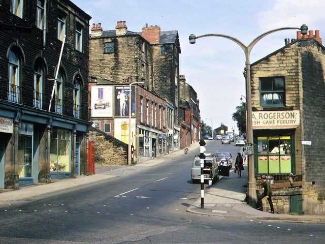 Chapel Hill from Morley Bottoms in August 1967. On the left hand side is the Conservative Club built in 1899 and three shops underneath. Beyond are the steps up to Bank Street and on to the Club fields of Cross Church Street Working Men's Club. After comes the cycle shop of John Hutchins and the base of the tall buildings which are also entered from Bank Street behind. Further up the hill are insurance offices and steps up to Bank Street. On the right hand side the photo shows the shop of Arthur Rogerson who took over the business of Baxter's fish, game and poultry merchants. This is the corner shop of a block that runs from 2 to 6 up Chapel Hill and 1 to 9 on Station Road. Some of the other buildings in this group had been demolished before they were listed.
