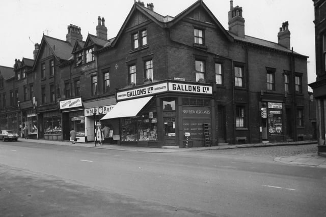 A parade of shops on Beeston Road with the junction with Marquis Street in July 1964. On the corner of Marquis Street is Gallons Ltd Provision Merchants where advertised in the windows are pork luncheon, eat at 1/9, fruit salad 1/4 and fresh butter at 2/3 a pound. A stripey 'barbers pole' on the corner points in the direction of Roy's Hairdressing Saloon for 'Haircuts'.