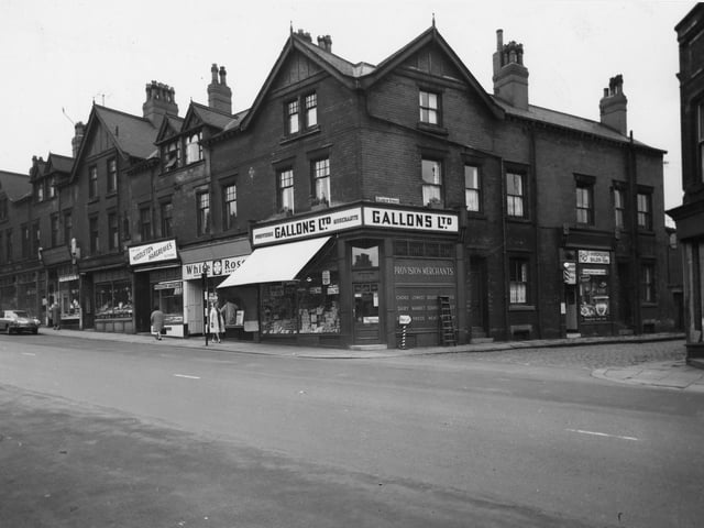 A parade of shops on Beeston Road with the junction with Marquis Street in July 1964. On the corner of Marquis Street is Gallons Ltd Provision Merchants where advertised in the windows are pork luncheon, eat at 1/9, fruit salad 1/4 and fresh butter at 2/3 a pound. A stripey 'barbers pole' on the corner points in the direction of Roy's Hairdressing Saloon for 'Haircuts'.