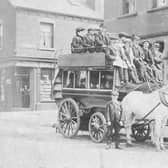 A horse-drawn omnibus stands outside the Bay Horse Hotel on Benson Place in June 1901. The omnibus, proprietor, John Thomas Bean & Son, is loaded with passengers on both the upper and lower deck. It is drawn by three horses. Mr. Bean, seated in the centre with whip, is dressed identically to the young man standing, most likely his son. They are wearing suits, cloth caps and are sporting button holes. The Bay Horse Hotel, at this time was run by Walter Newbould. The shop in the background, left is at the corner with Woodhouse Hill Terrace and is numbered 14 Woodhouse Hill Road, The Central Drug Store. The lettering on the side of the omnibus says 'Briggate' and 'Hunslet Carr'.