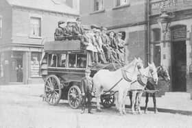 A horse-drawn omnibus stands outside the Bay Horse Hotel on Benson Place in June 1901. The omnibus, proprietor, John Thomas Bean & Son, is loaded with passengers on both the upper and lower deck. It is drawn by three horses. Mr. Bean, seated in the centre with whip, is dressed identically to the young man standing, most likely his son. They are wearing suits, cloth caps and are sporting button holes. The Bay Horse Hotel, at this time was run by Walter Newbould. The shop in the background, left is at the corner with Woodhouse Hill Terrace and is numbered 14 Woodhouse Hill Road, The Central Drug Store. The lettering on the side of the omnibus says 'Briggate' and 'Hunslet Carr'.