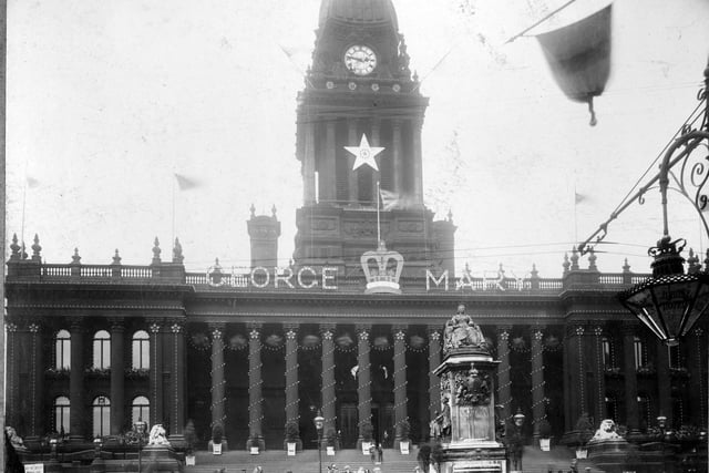 Leeds Town Hall, decorated for the coronation of King George V and Queen Mary in June 1911. The names of the George and Mary are on the top of the building, with a crown. Lights circle the pillars and dome. In front of the Town Hall is the statue of Queen Victoria, which was removed to Woodhouse Moor in 1937.