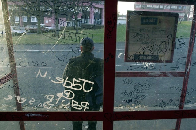 A bus passenger waits at a vandalised stop on Gamble Hill in October 2003.