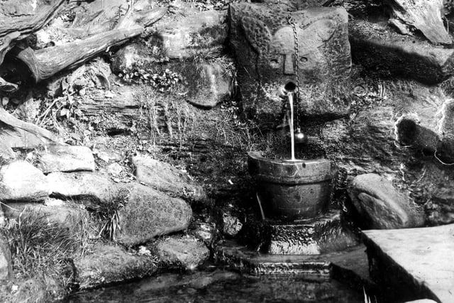 The Dog's Mouth Spring, Old Well and Drinking Cup. The source of this spring was at the southern end of Great Heads Beck which flowed through the Gorge, a wooded area of Roundhay Park. The water springs from the mouth of a dog's head, roughly carved in the rock face, hence Dog's Mouth Spring. A copper drinking cup is suspended from a chain for thirsty wanderers.