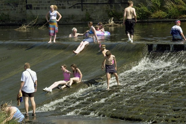 Basking in the glorious sunshine and high temperatures in July 2003 are visitors to Otley sliding down the weir in the River Wharfe, and cooling off in the river.