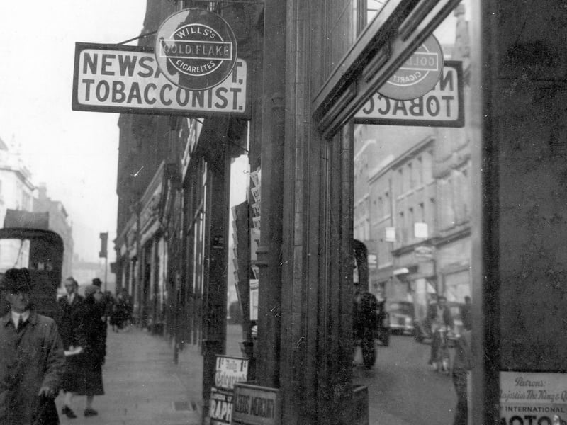 Albion Street in September 1937 showing Jowett and Sowry, Swift Bros. debt collectors, tobacconist with sign for Gold Flake, Players and newspaper placard outside. Also in view are people walking along street and Headrow buildings in the distance.