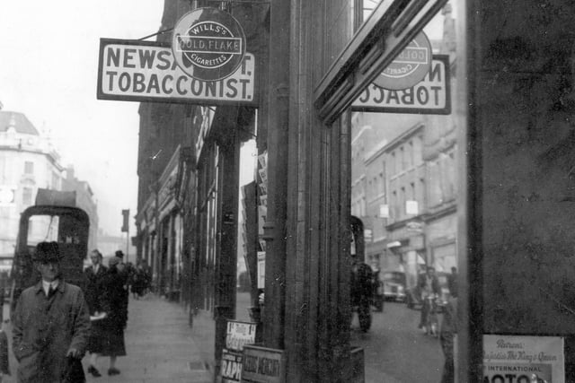 Albion Street in September 1937 showing Jowett and Sowry, Swift Bros. debt collectors, tobacconist with sign for Gold Flake, Players and newspaper placard outside. Also in view are people walking along street and Headrow buildings in the distance.