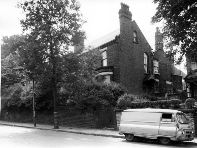 A view through trees in full leaf of an imposing brick built detached house of substantial size on Beeston Road. The house has two bay windows and is in an elavated position set back from the road. The front gate leads left up steps to the front entrance or straight up another set of steps to the side entrance.