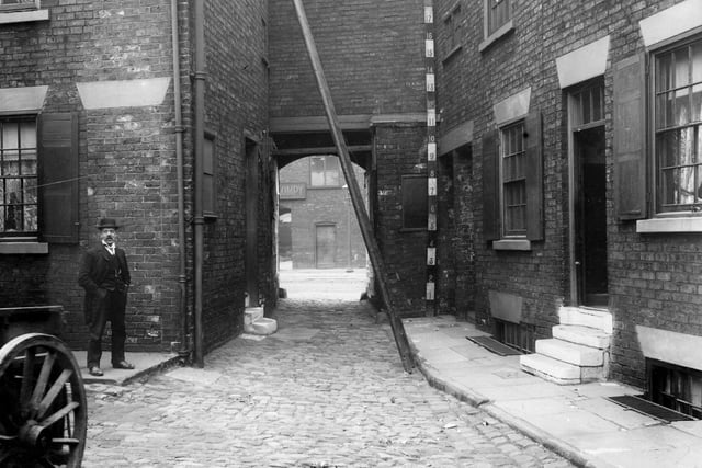 Houses in Francis Court, set around cobbled yard. Access was from Neville Street, entrance between number 13 and 14. A measuring rod and ladders are near the entrance, a workman looking on, dressed in the fashion of the period. Through the entrance a portion of School Close Mills can be seen, which was at number 26 Neville Street, on the opposite side. Pictured in September 1910.