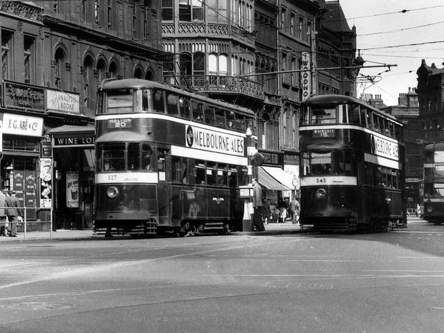 Trams on Boar Lane in  July 1953. No.527 in front is on route 20 to Halton, while no.545 is on route 15 to Whingate. In the background is tram no.275. Shops on the left include Tatler cinema, F.G. Abe & Co., stationers and printers, and Albert Cowling's Wine Lodge.
