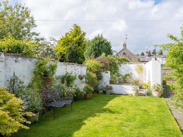 This lawned garden lies to the rear with a seating area and mature trees and shrubs.