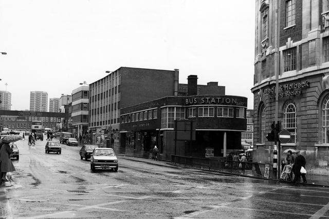 A view looking north along Vicar Lane showing the bus station in the centre. On the right is the Leeds & Holbeck Building Society next to the junction with Lady Lane. It is a wet day and several people can be seen with umbrellas.