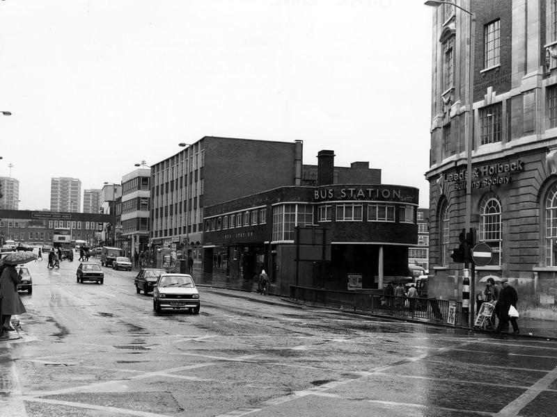 A view looking north along Vicar Lane showing the bus station in the centre. On the right is the Leeds & Holbeck Building Society next to the junction with Lady Lane. It is a wet day and several people can be seen with umbrellas.