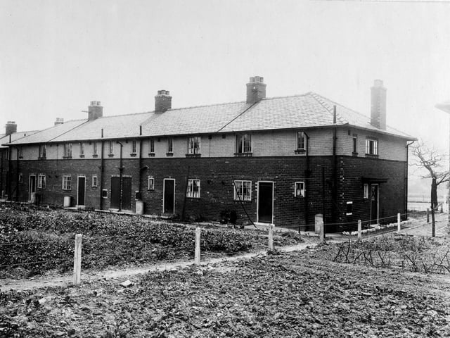 The Wyther housing estate pictured in June 1921. The row of houses are numbered 21-27. A large area in front of the houses has been turned into an area where the residents can plant things. The houses are newly built two storey buildings. An outhouse is placed in the middle of the four houses.