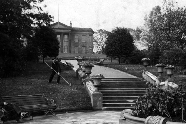 A man is tending to the grass while another man relaxes on a bench in this postcard view of The Mansion. It is postmarked October 27, 1908.