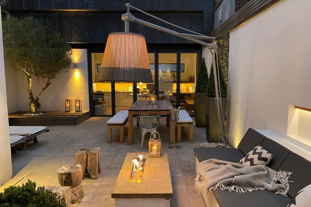 The rear Mediterranean style courtyard with Yorkshire stone patio has a fitted teak breakfast bar.  Bay seating and a coffee table with bio fuel fire pit, along with a raised olive tree, make this a lovely outdoors area.