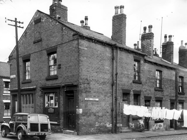 Back-to-back built terraced houses in Ambro Street. A line of terry nappies is strung across the road at number 1. At number 16 Kiln Street is a fish and chip shop, boasting the purest dripping, with the opening times displayed outside. A Morris 1000 is parked on Kiln Street and far right is Algeria Street.
