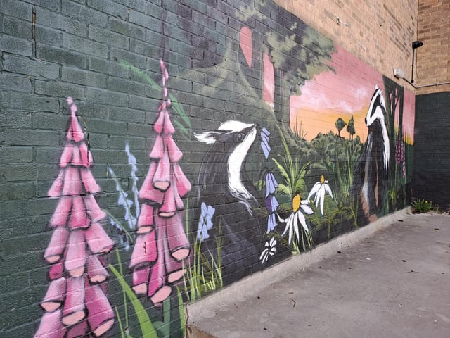 A mural showing badgers playing among flowers and trees under a beautiful sunset at The Gaunt shopping precinct in Gleadless Valley