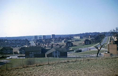 Kentmere Avenue running from left to right showing the rear of The Gate Hotel pub in the centre in the late 1960s. Towards the right is the junction with Ramshead Hill, leading off to the right, and Boggart Hill Drive, leading left then up into the distance towards the tower blocks of Barncroft Grange, Barncroft Court, Barncroft Towers and Barncroft Heights. Grange Farm Infant School is in the centre.