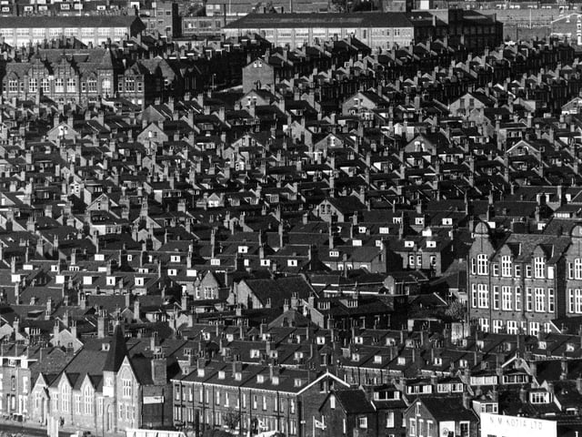 An aerial view over Chapeltown and Harehills from Roseville Road, part of which is seen in the bottom left-hand corner. Roseville Works is visible at the bottom edge. The camera looks across an area densely populated with red brick streets. On the right, the large brick building with decorative gables is the former Kepler Council School which was later known as Roseville County Secondary School.  Another school is visible towards the top left. It has two towers with pointed roofs and dutch-style gables. This is the former Gipton Board School, built in 1897, and fronting Harehills Road between Conway Street and Conway Mount. It became Harehills County Secondary School and the Harehills Middle School.