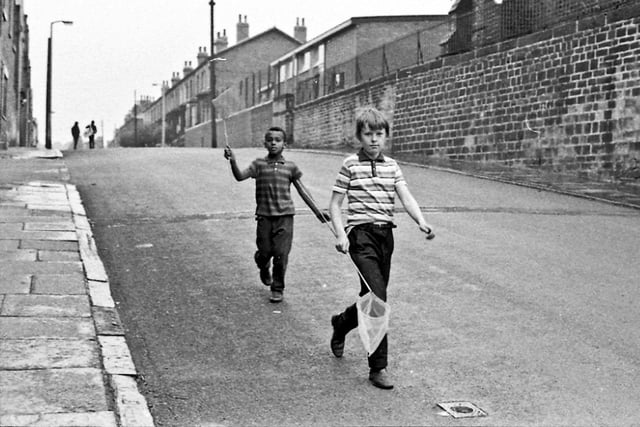Two young boys make their way down King's Road brandishing their fishing nets. They are both looking directly at the camera. On the right is a high stone-built wall, behind which are All Hallows' C of E Church and Parish Hall.
