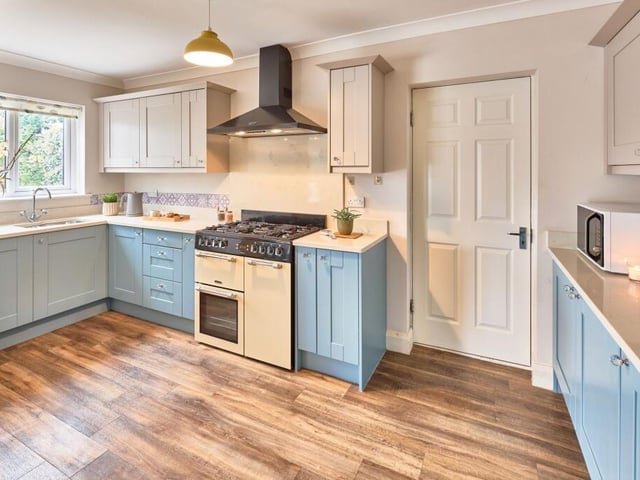Within the kitchen, two tone blue and neutral shaker style cabinetry are paired with fresh Quartz worktops that continue seamlessly up the wall to form the splashback behind the traditional Cookmaster range oven.