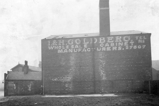 Side view of derelict property of I and H Goldberg cabinet manufacturers of Sheepscar Street South and North Street. A man is holding a surveyor's measure against the building. There is a poster for the Newtown Picture Palace on the wall and a street lamp on the corner. Pictured in March 1934.