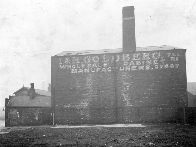 Side view of derelict property of I and H Goldberg cabinet manufacturers of Sheepscar Street South and North Street. A man is holding a surveyor's measure against the building. There is a poster for the Newtown Picture Palace on the wall and a street lamp on the corner. Pictured in March 1934.