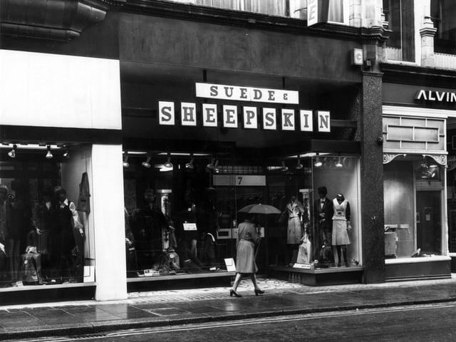 A woman with an umbrella walks along King Edward Street in May 1976. The Suede and Sheepskin shop is in view. To the right is Alvin Morris Ltd., decorators' supplies showroom.