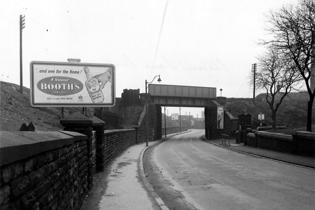 Looking north east shows the railway bridge over Oldfield Lane in March 1956. Trees and an entrance to Wortley recreation ground can be seen to the right. An advertisement for Booth's dry gin is on the left in the foreground and one for Turog bread is to the right of the bridge.