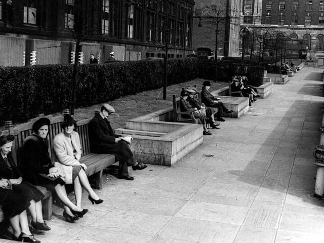 A view looking east along the Garden of Rest between the Headrow and Centenary Street, towards Cookridge Street in September 1943. Members of the public sit on the large benches in front of a hedge. Behind the hedge are the Municipal Buildings (Library, Art Gallery and Police H.Q.). Air raid protection around ground floor of Municipal Building.