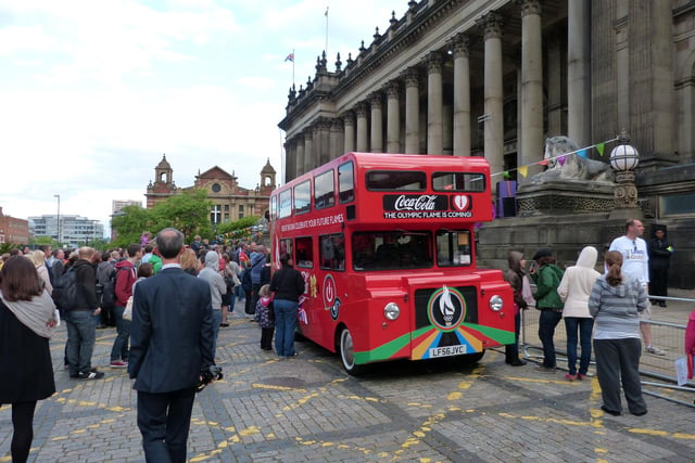 Crowds gathered outside Leeds Town Hall to greet the first of the Olympic torchbearers to carry the flame on its journey through the city centre. Parked in front is the red Coca Cola sponsored, double decker Olympic Torch Tour Bus. The Town Hall is to the right with Oxford Place Chapel behind the trees in the background.