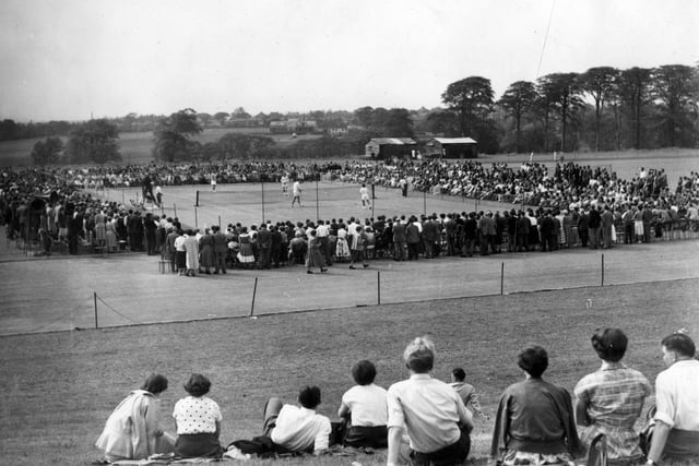 An exhibition tennis match in progress at the Temple Newsam Arena. The players taking part in this mixed doubles match are Miss Doris Hart (USA) and Roger Becker (GB) versus Miss Lois Felix (USA) and Hugh Stewart (USA). Crowds of spectators are gathered all around the court to get a close-up view while others are sitting on the grassy hill in the foreground to look down on the action.