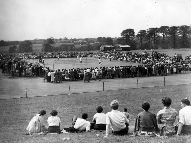 An exhibition tennis match in progress at the Temple Newsam Arena. The players taking part in this mixed doubles match are Miss Doris Hart (USA) and Roger Becker (GB) versus Miss Lois Felix (USA) and Hugh Stewart (USA). Crowds of spectators are gathered all around the court to get a close-up view while others are sitting on the grassy hill in the foreground to look down on the action.