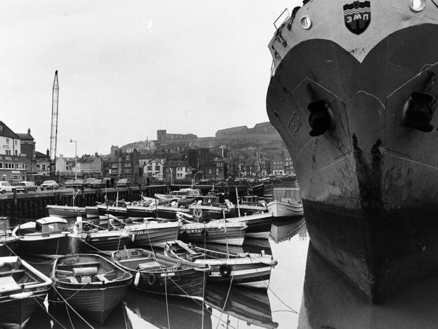 A cluster of cobles and motor boats dwarfed by the bows of ship OTEPYA which is taking on 1,000 tons of barley for Tallinn in Estonia. Pictured in April 1972.
