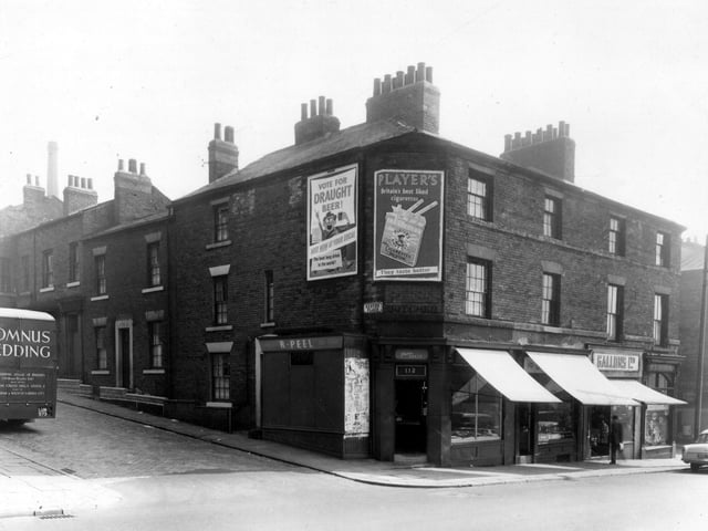 Woodhouse Lane in August 1959. Exeter Place is on the left, a delivery truck carrying Somnus Bedding is visible. It was produced by William Rhodes Ltd, of Carlton Cross Mills. Number 112 Woodhouse Lane is a butchers shop, business of Eric Peel. Moving right, 110 is also a butcher, specialising in pork products, D. Addyman. A branch of Gallons Ltd, grocers is at 108. On the right, at the corner with Exeter Street is Frank Clude Stock, chemist.