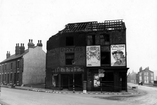 Derelict shops on the corner of Gelderd Road and Wortley Lane in February 1943. Advertisements for Heinz and Ovaltine visible. Road signs for the North East and York. A streetlamp can be seen.