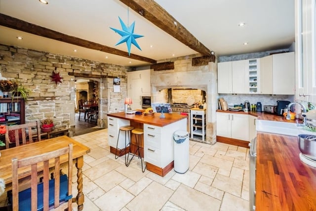 A large family kitchen with underfloor heating has a central island, and a stone fireplace housing a range style cooker.