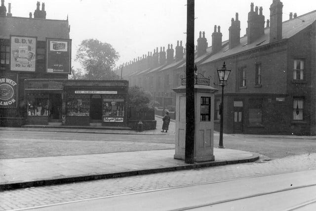 Telephone box at the junction of Cardigan Road and Thornville Road in June 1936. Behind the telephone box, across the street, can be seen two shops. At number 2 is a drapers shop and 2a The Albert, tobacco, chocolates, stationery. There is a street lamp to the right of the photo. Above and to the side of the drapers shop are large advertising hoardings