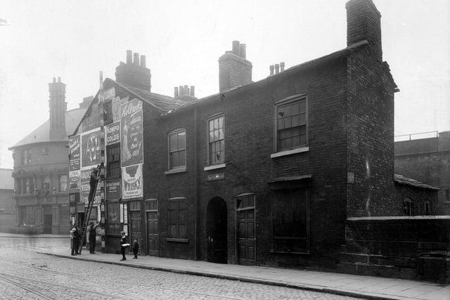 York Street at the junction with Duke Street in July 1907. The ornate facade of the Lloyds Arms public house is on Duke Street, to the left. It was demolished in 1994 to build the inner city loop road. Workmen are measuring shop property, this was number 48 York Street, run by Sarah Ann Curtis.