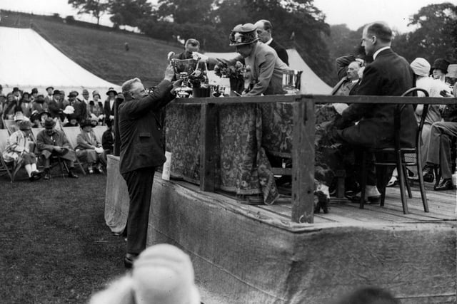 The Lady Mayoress, Ella Lupton presents a silver cup at Leeds Flower Show held at Roundhay Park in July 1927. Seated on the dais with his back to the camera is the Director of the City Art Gallery, S.C. Kaines Smith. Marquees have been put up in the park to display the flowers.