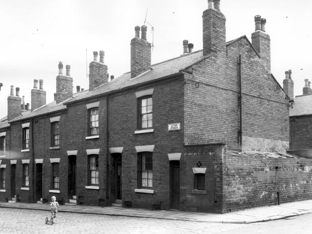 A small boy rides his scooter on Acton Street from the junction with Kiln Street. The end door and window on the right are those of a block of several outside toilet facilities for the use of the street. It was an area designated for clearance in line with the Housing Act of 1957.