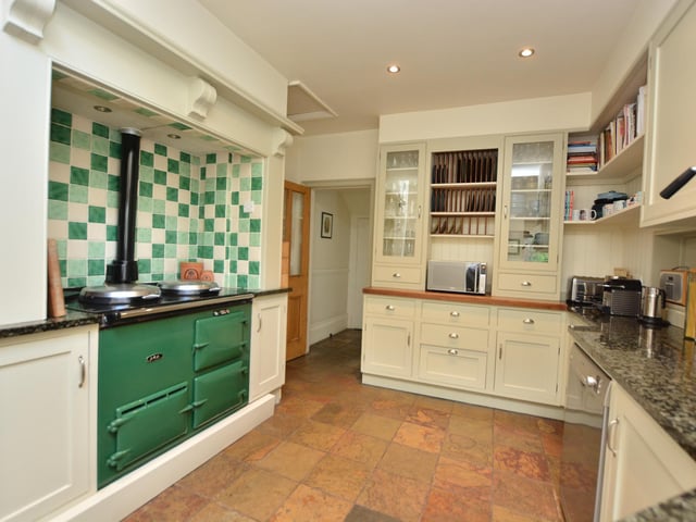 The kitchen has a well-designed layout with traditional cabinetry, some glass fronted units and a peninsular divider separating the breakfast space.