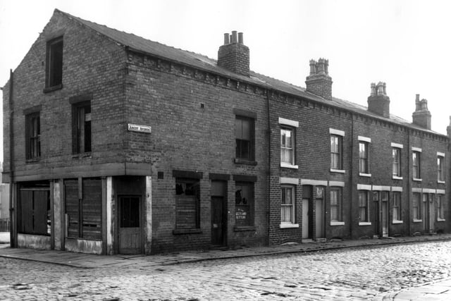 Ascot Street in October 1966. The boarded up remains of a belts and buttons shop on the left and a row of through terraced houses on the right. The road on the far left is Cross Ascot Street.