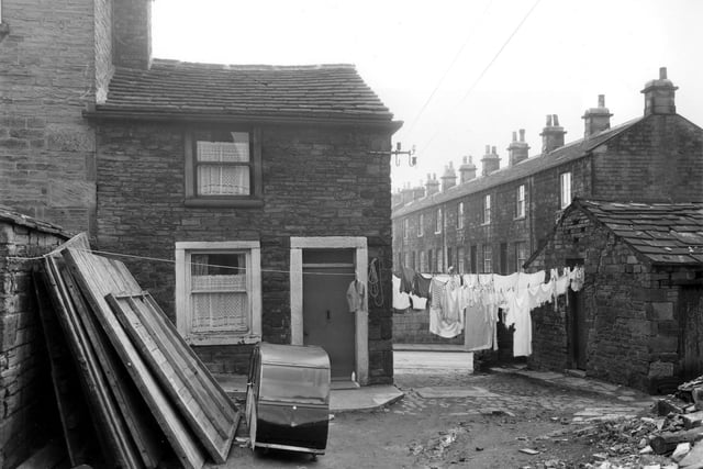 A line of washing stretches across the narrow entrance to Bell Lane. The dwelling in the foreground is number 7 Barker's Place. Timber fencing panels lean against a wall beside a sidecar parked in the yard. Pictured in April 1960.
