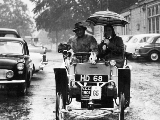 Sheltered under an umbrella, Major James France and his wife take their 1901 Clement Panhard through pools of water on their way to the Concours D'Elegance event of the Veteran Car Rally at Harrogate in September 1961.