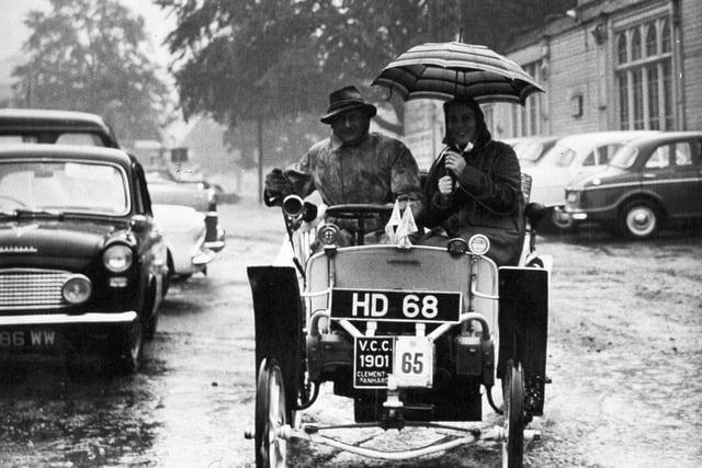 Sheltered under an umbrella, Major James France and his wife take their 1901 Clement Panhard through pools of water on their way to the Concours D'Elegance event of the Veteran Car Rally at Harrogate in September 1961.