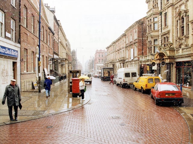 Albion Place, seen from the junction with Albion Street, in February 1991. On the left is Dacre, Son & Hartley, estate agents. On the right, Austin Reed menswear occupies part of the old YMCA building. Cars and vans are parked on the road. It is a wet day and shoppers are carrying umbrellas.