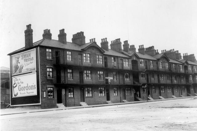Marsh Lane tenements, built in 1901 by private developer, one of the first steps towards redevelopment run down, unhealthy inner city housing. Three storey blocks of flats in groups of twelve and fifteen, staircases provided access to balconies. First ground floor unit to left is a shop. Advertisements on wall feature 'Swan Vestas' matches and 'Gordons' Gin'. Pictured in August 1939.
