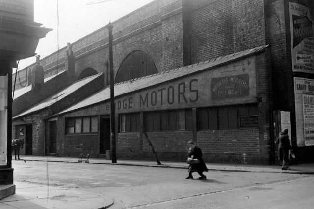 Willoughby Crescent in  May 1951.  In focus are vacant premises in the railway arch of bridge motors. The building awaits conversion by Purvis Logs. On the corner are bill posters for the Grand Theatre and Hemingways Ltd. furnishers at the Headrow. Two women crossing the street. A horse is half visible to the left.